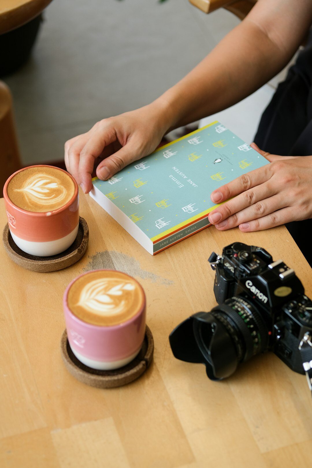 Hands holding a film camera and notebook on a cafe table